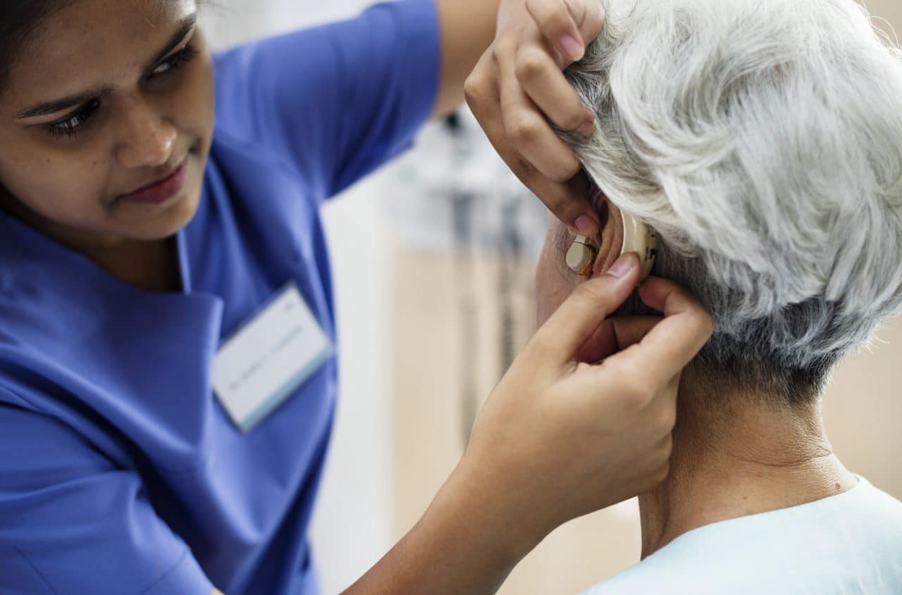 An older woman getting fitted with a hearing aid.