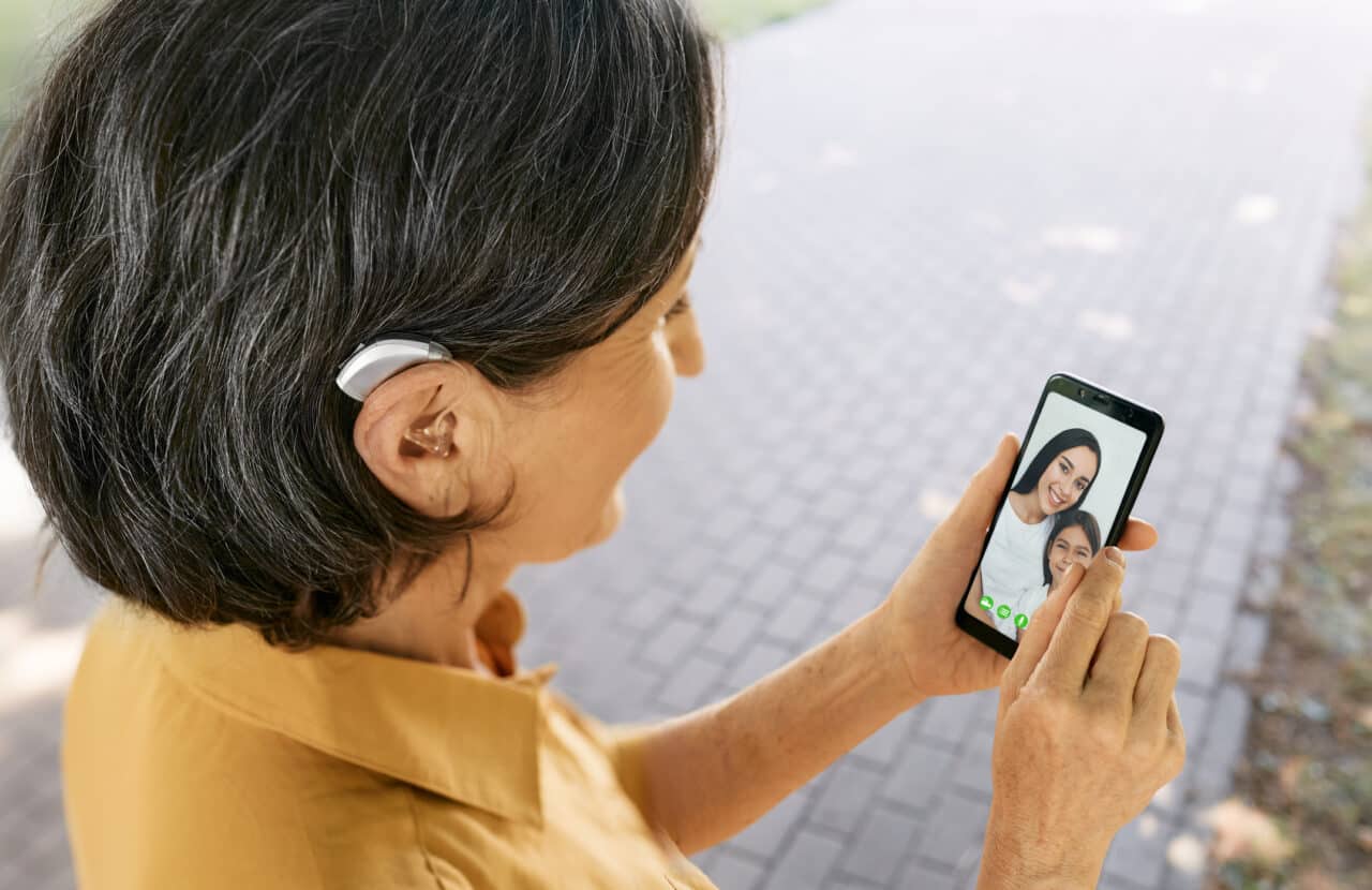 Woman with a hearing aid FaceTiming with family on her smartphone.