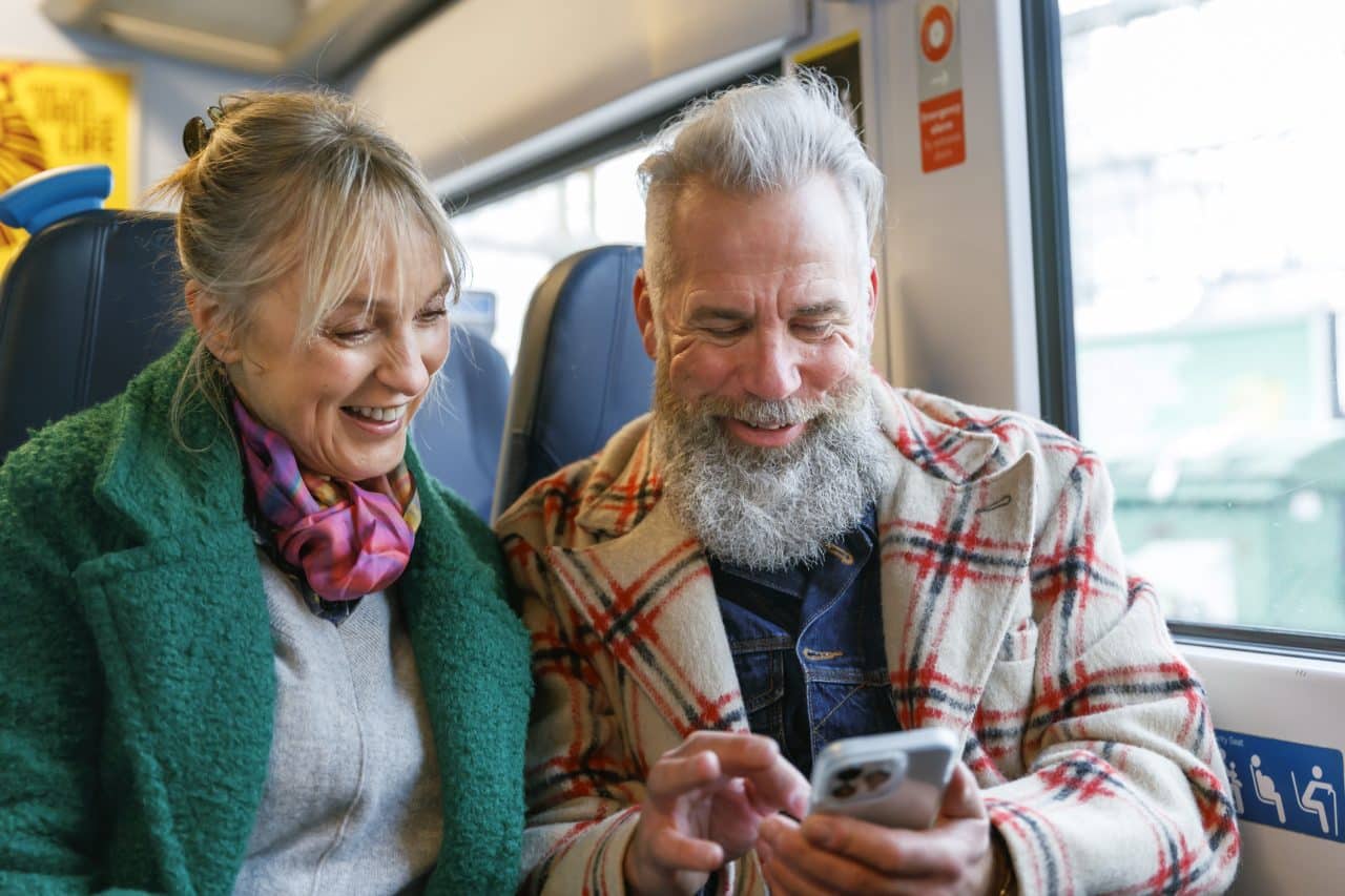 An adventurous senior couple on vacation check their travel itinerary on a smart phone while riding a train.