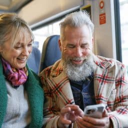 An adventurous senior couple on vacation check their travel itinerary on a smart phone while riding a train.