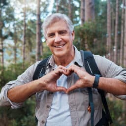 Man in the woods forming a heart in front of him with his hands