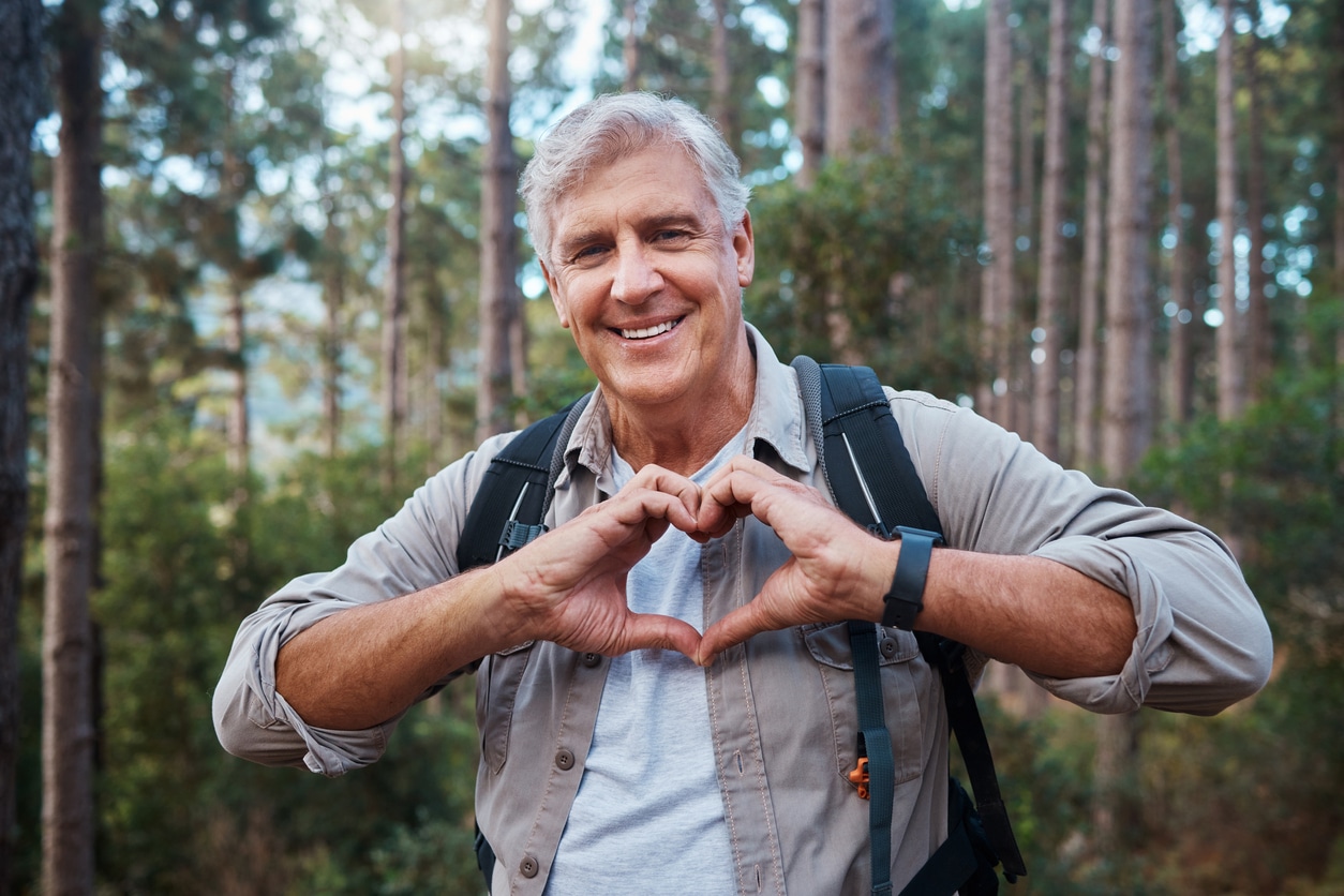 Man in the woods forming a heart in front of him with his hands